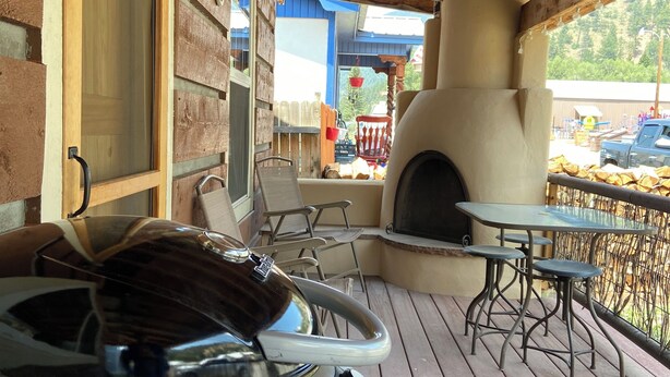 Een terras buiten met een barbecue, een tafel met stoelen en een pizzaoven.