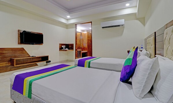 Habitación de hotel con dos camas, televisión, armario de madera y aire acondicionado.