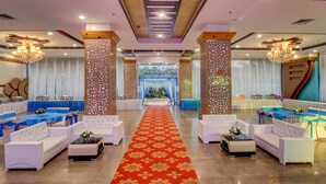 Un amplio vestíbulo de hotel con alfombra roja, sofás blancos y mesas azules.