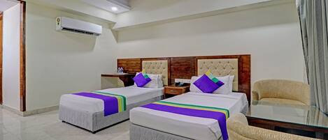 Habitación de hotel con dos camas, un sofá, una mesa de vidrio y un equipo de aire acondicionado.