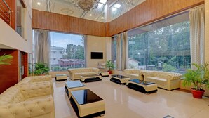 Un salón amplio con ventanas grandes, un televisor de pantalla plana y varios sofás y mesas auxiliares.