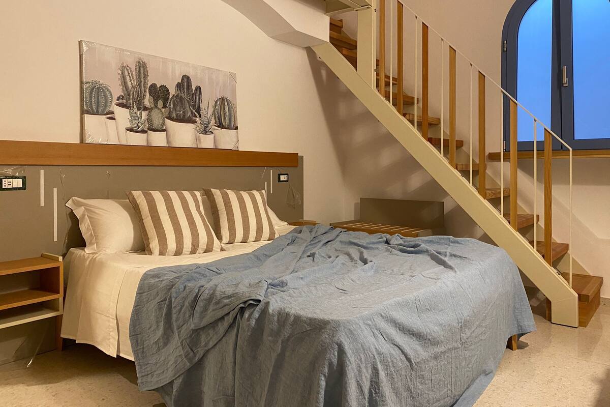 A bedroom with a bed, a staircase, and a window.