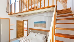 A bedroom with a bed, wooden headboard, a painting of a beach, a staircase, and a door. - La Corte Residence (Salve)