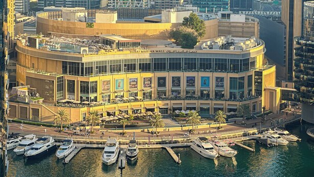 A waterfront building with multiple balconies, a marina with yachts, and a prominent sign for Dubai Marina Mall.