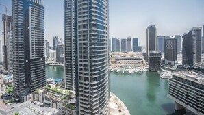 A high-rise building with a curved facade, a marina with boats, and other modern skyscrapers in the background.