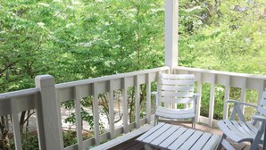 A wooden deck with white chairs and a table, surrounded by lush greenery.