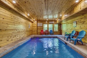 An indoor swimming pool with wooden walls and ceiling, surrounded by chairs. - A Lasting Impression cabin- private indoor pool and incredible views! (Sevierville)