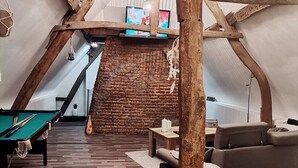 Een zolderkamer met een pooltafel, een bank en een bakstenen muur.