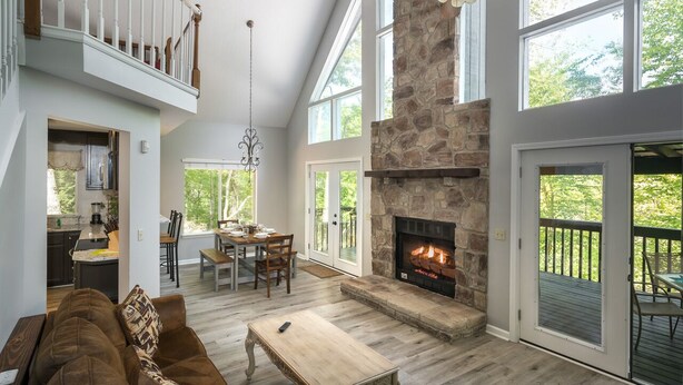 A spacious living room with a stone fireplace, a dining area, and a kitchen visible through an open door. - Home theater, hot tub, pool table, secluded, spacious. (Gatlinburg)