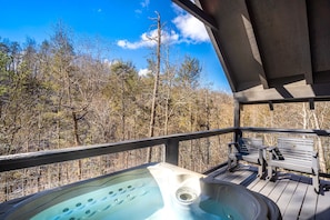 A hot tub on a wooden deck with benches, surrounded by trees. - Cozy and Comfortable. Hot tub on your Private Deck. (Gatlinburg)