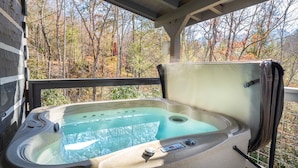 A hot tub on a covered deck with a view of autumn trees.
