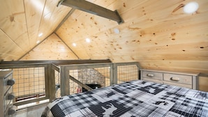 A wooden cabin interior with a bed, a window, and a staircase.