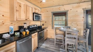 A wooden cabin kitchen with a dining area, featuring wooden cabinets, a microwave, a coffee maker, and a dining table with chairs.
