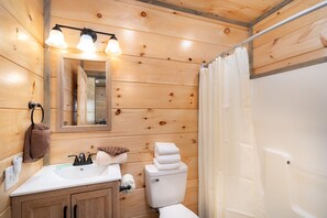 Ein Badezimmer mit Holzwandverkleidung, Waschbecken, Spiegel und Toilette.