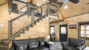 A wooden cabin interior with a staircase, two leather sofas, a table, and a door.
