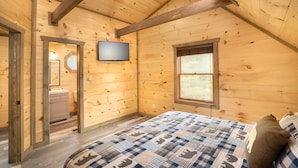 Ein Zimmer in einer Holzhütte mit einem Bett, einem Fernseher, einem Fenster und einer Tür zu einem Badezimmer.