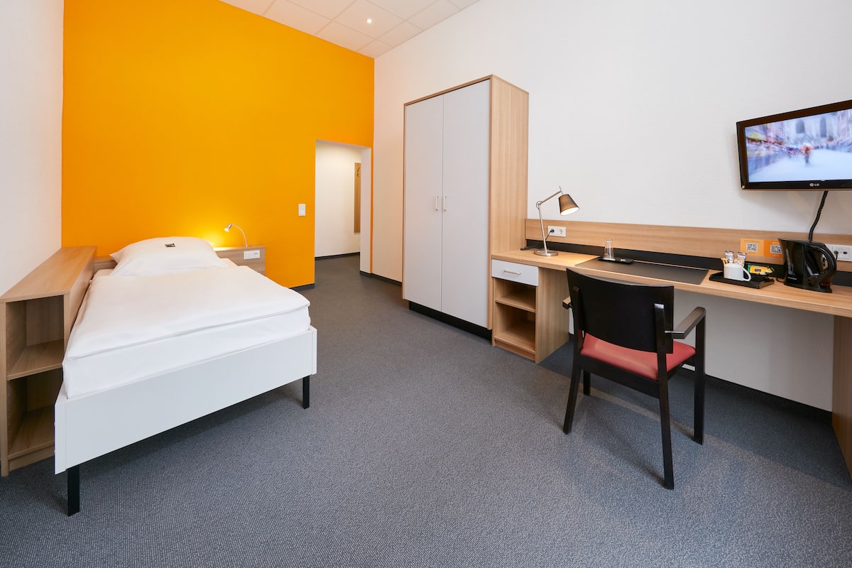 A hotel room with a bed, desk, chair, TV, and wardrobe.