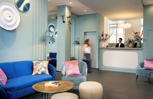 Un moderno vestíbulo de hotel con un sofá azul, un mostrador de recepción y una mesa de centro con un libro.