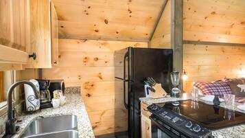 A compact kitchen with wooden walls, a stainless steel sink, a black refrigerator, and a stove.