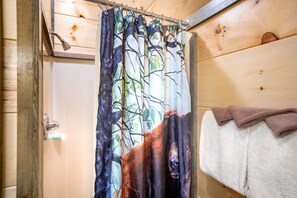 A bathroom with a shower curtain featuring a forest print, a towel rack with a folded towel, and wooden paneling on the walls.