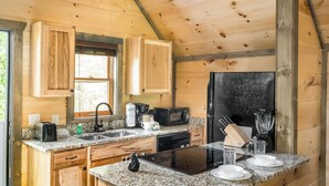 Una cocina compacta con armarios de madera, encimera de granito, refrigerador negro y cafetera.