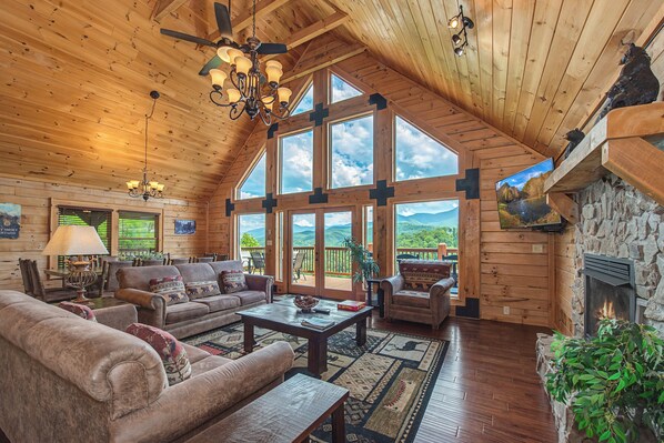 L’intérieur d’une cabane en rondins, avec une cheminée, de grandes fenêtres et un coin salon confortable.