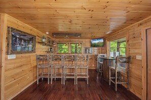 Un intérieur en bois avec un coin bar, plusieurs chaises et un téléviseur.