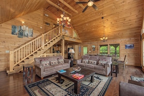L’intérieur d’un chalet en bois, avec un escalier, deux canapés, une table basse et un lustre.