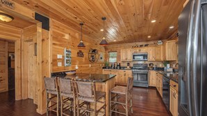 Una cucina in stile baita con pareti in legno, un'isola centrale con sgabelli da bar, elettrodomestici in acciaio inossidabile e una lampada a sospensione.