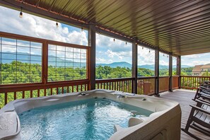 Un bain à remous sur une terrasse en bois, avec de grandes fenêtres donnant sur un paysage montagneux.