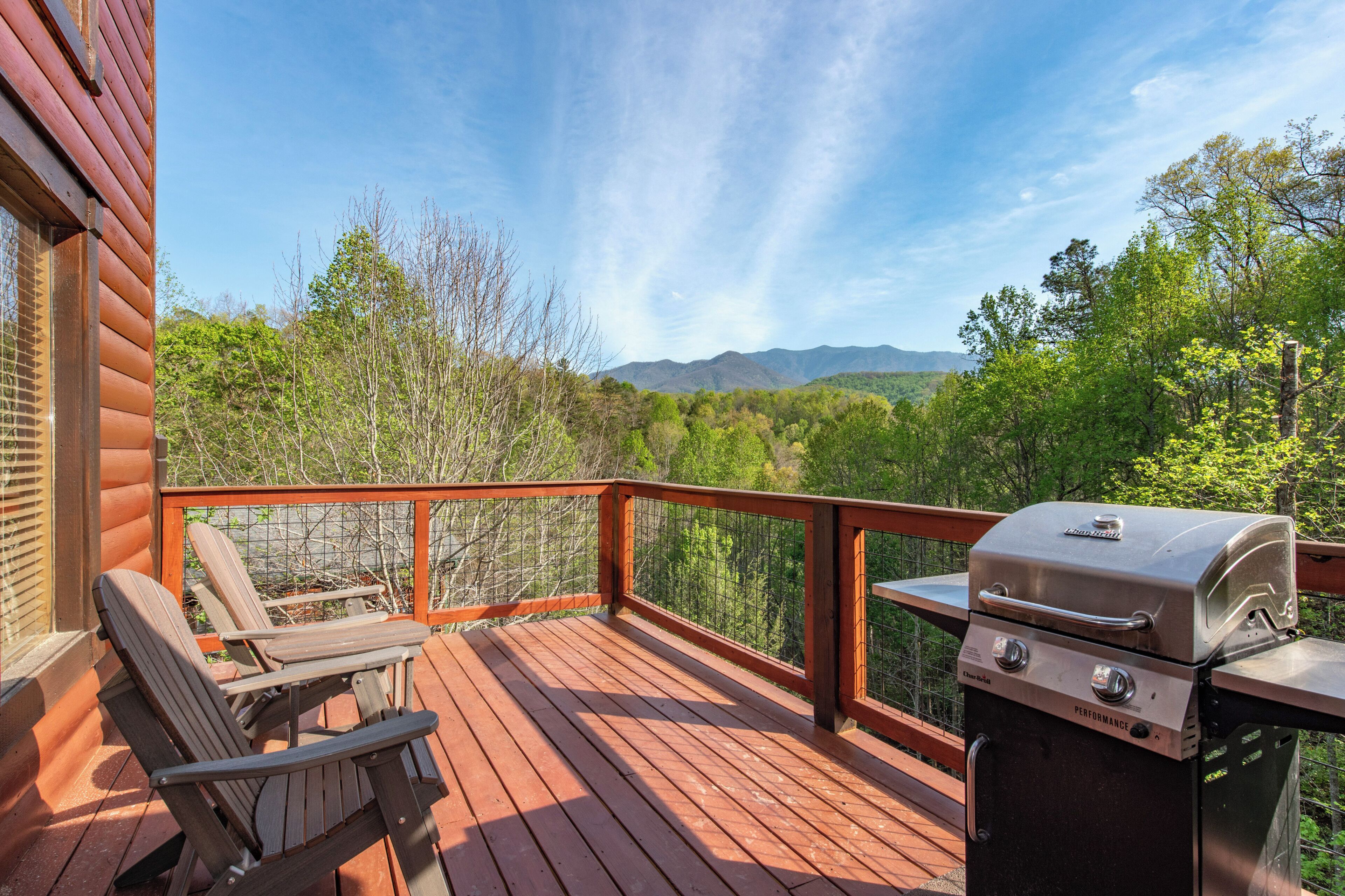 Une terrasse en bois avec un barbecue et des chaises, donnant sur une zone boisée.