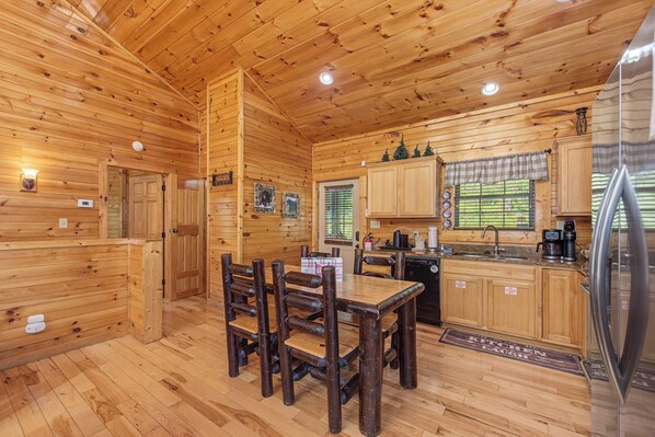 Interior de una cabaña de madera con una mesa de comedor, sillas, una zona de cocina y un refrigerador.