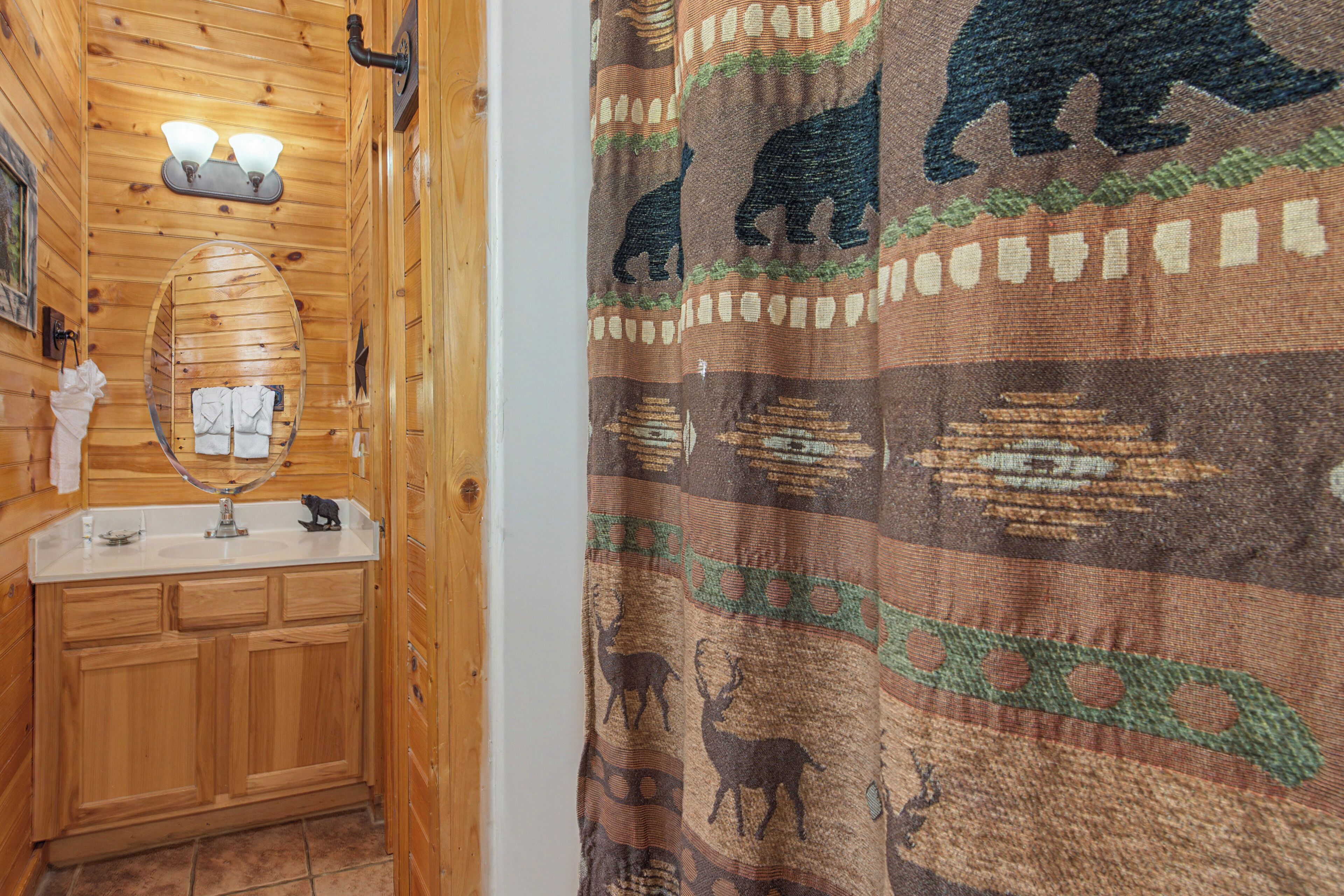 A wooden cabin bathroom with a sink, mirror, and a bear-themed shower curtain.