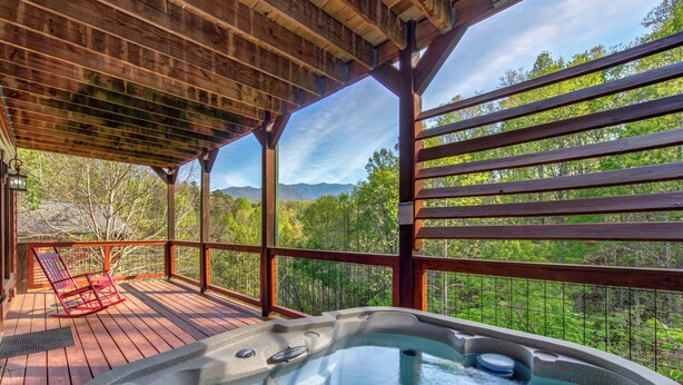 Un jacuzzi en una terraza de madera con vistas a montañas y árboles.