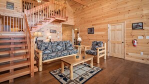 A wooden cabin interior with a staircase, a sofa, two chairs, a coffee table, and a rug. - 2 King Bedrooms, Jetted Tubs, Screened in Porch, Private Hot tub, Pet Friendly (Gatlinburg)