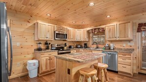 A modern kitchen with wooden paneling, stainless steel appliances, and a central island with stools. - 2 King Bedrooms, Jetted Tubs, Screened in Porch, Private Hot tub, Pet Friendly (Gatlinburg)