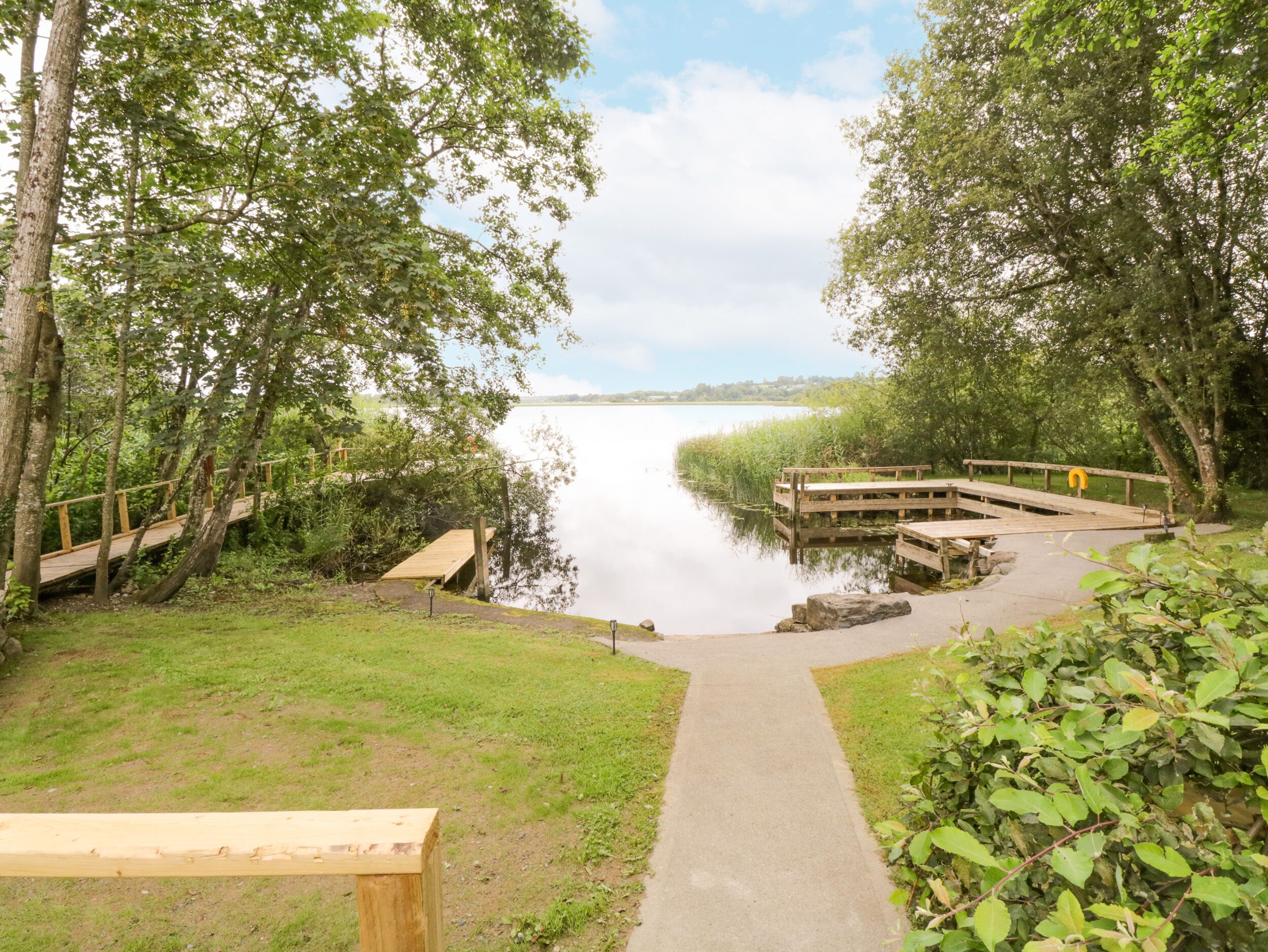 A wooden dock extending into a calm lake, surrounded by lush greenery and a clear sky.