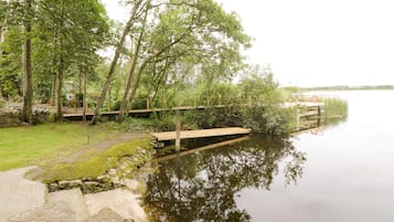 A calm lake with a wooden dock extending into the water, surrounded by lush greenery and trees.
