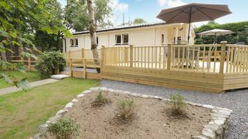 Eine Holzterrasse mit Geländer, ein überdachter Patio-Bereich mit Tischen und Stühlen sowie ein Garten mit kleinen Pflanzen und einem Kiesweg.