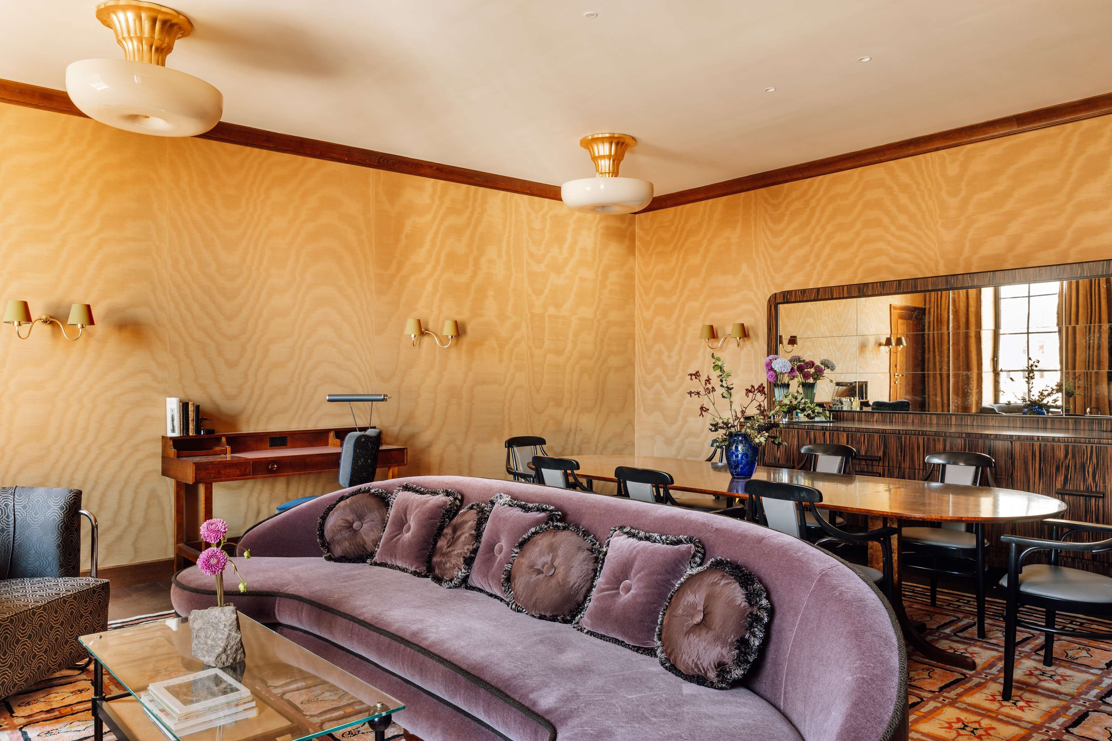 Una habitación de hotel moderna con un sofá morado acolchado, una mesa de comedor de madera y un espejo grande.