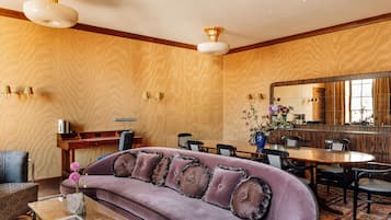Una habitación de hotel moderna con un sofá morado acolchado, una mesa de comedor de madera y un espejo grande.