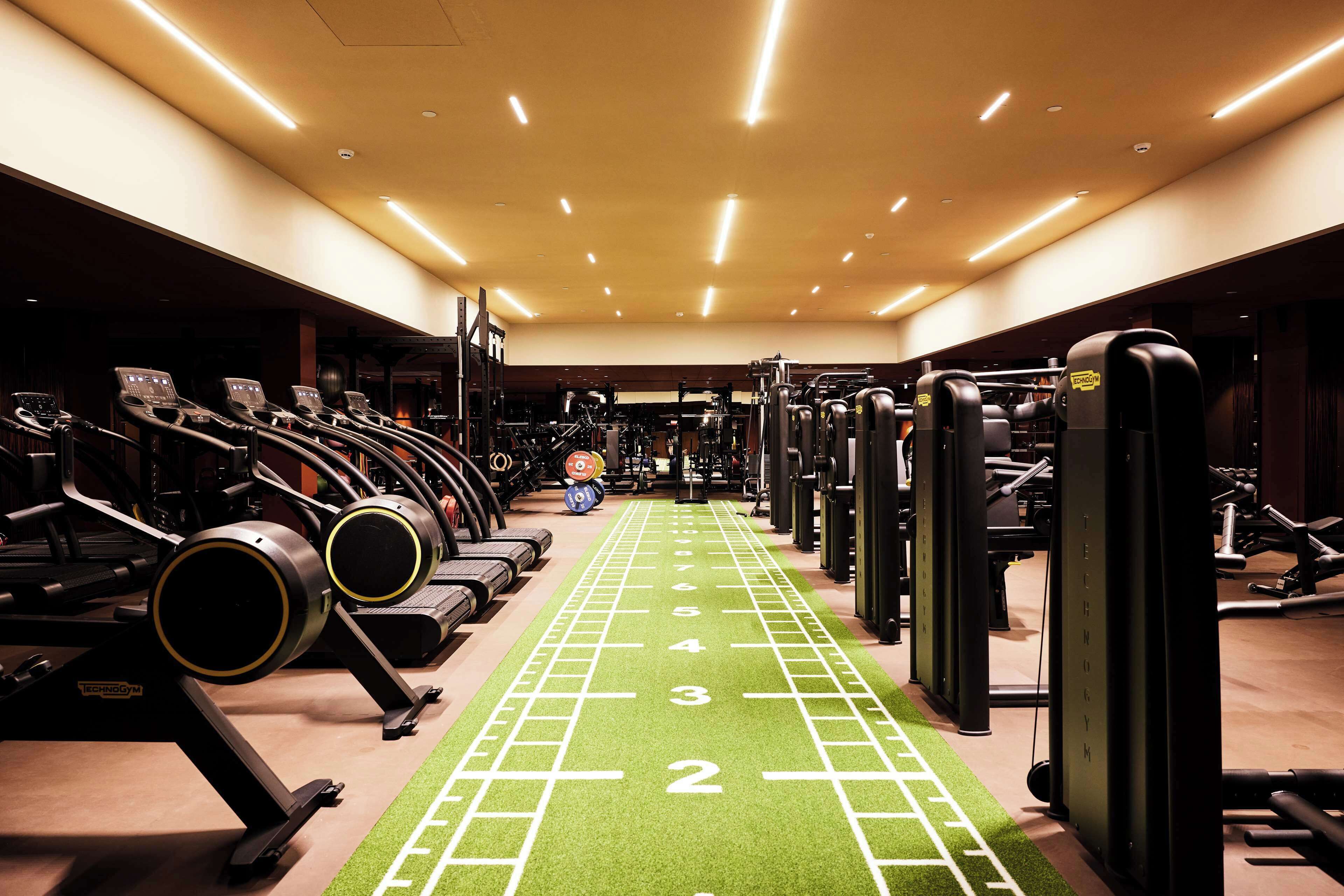 Un gimnasio con cintas de correr, máquinas de pesas y una pista de atletismo verde.
