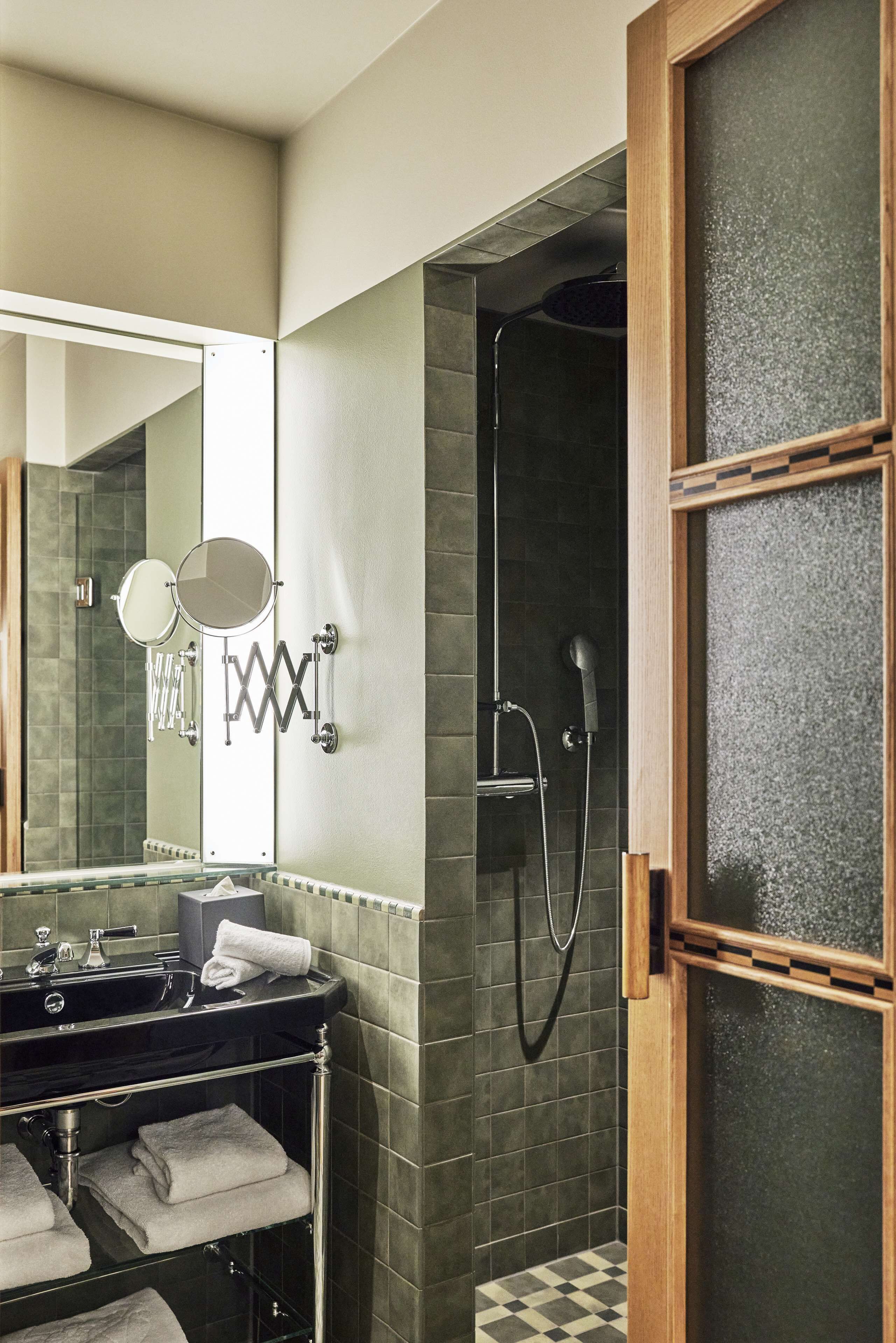 Un baño moderno con un lavabo negro, dos espejos, una ducha y un área de ducha con paredes de vidrio.