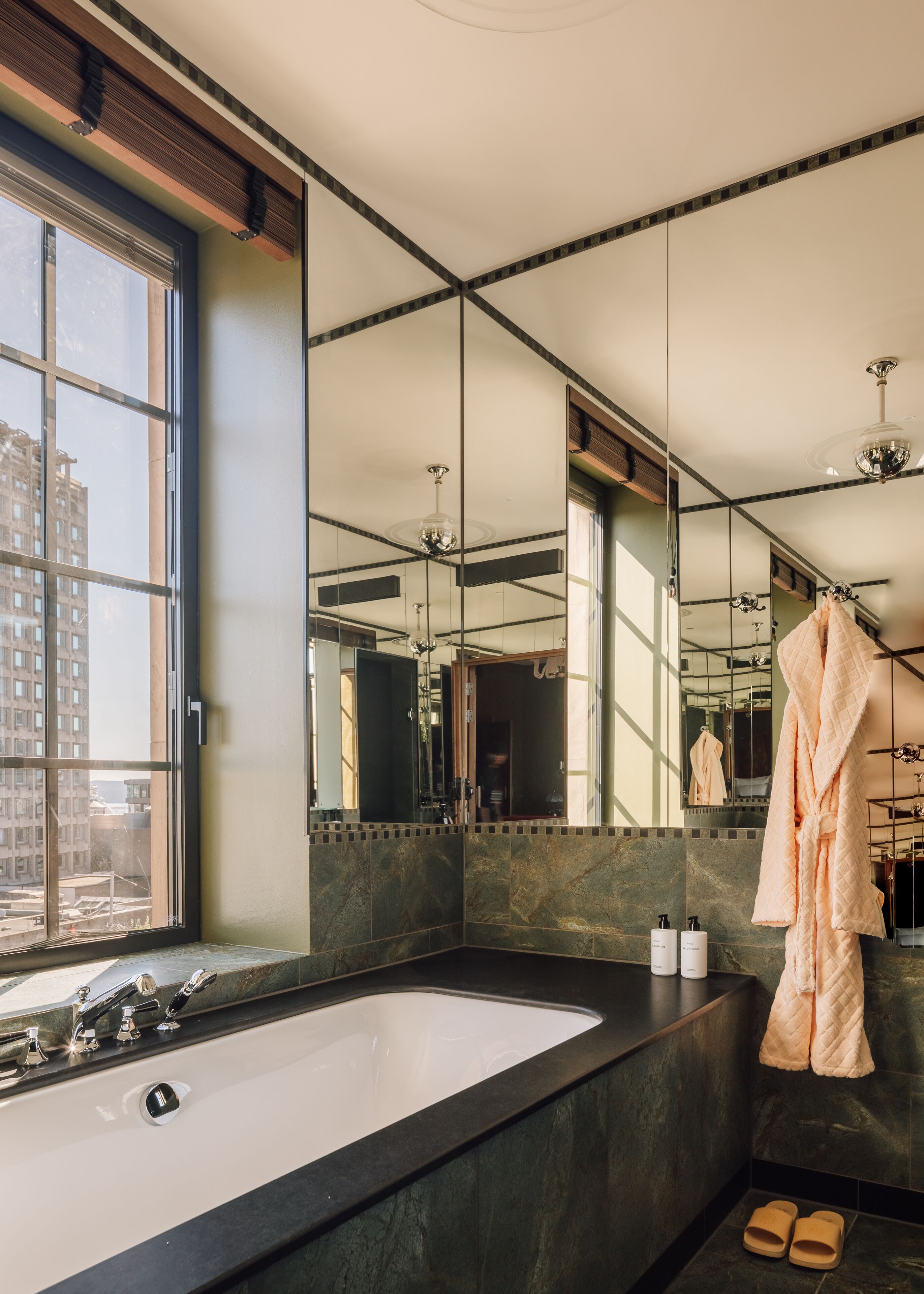 A modern bathroom with a large mirror, a bathtub, and a window overlooking a cityscape.