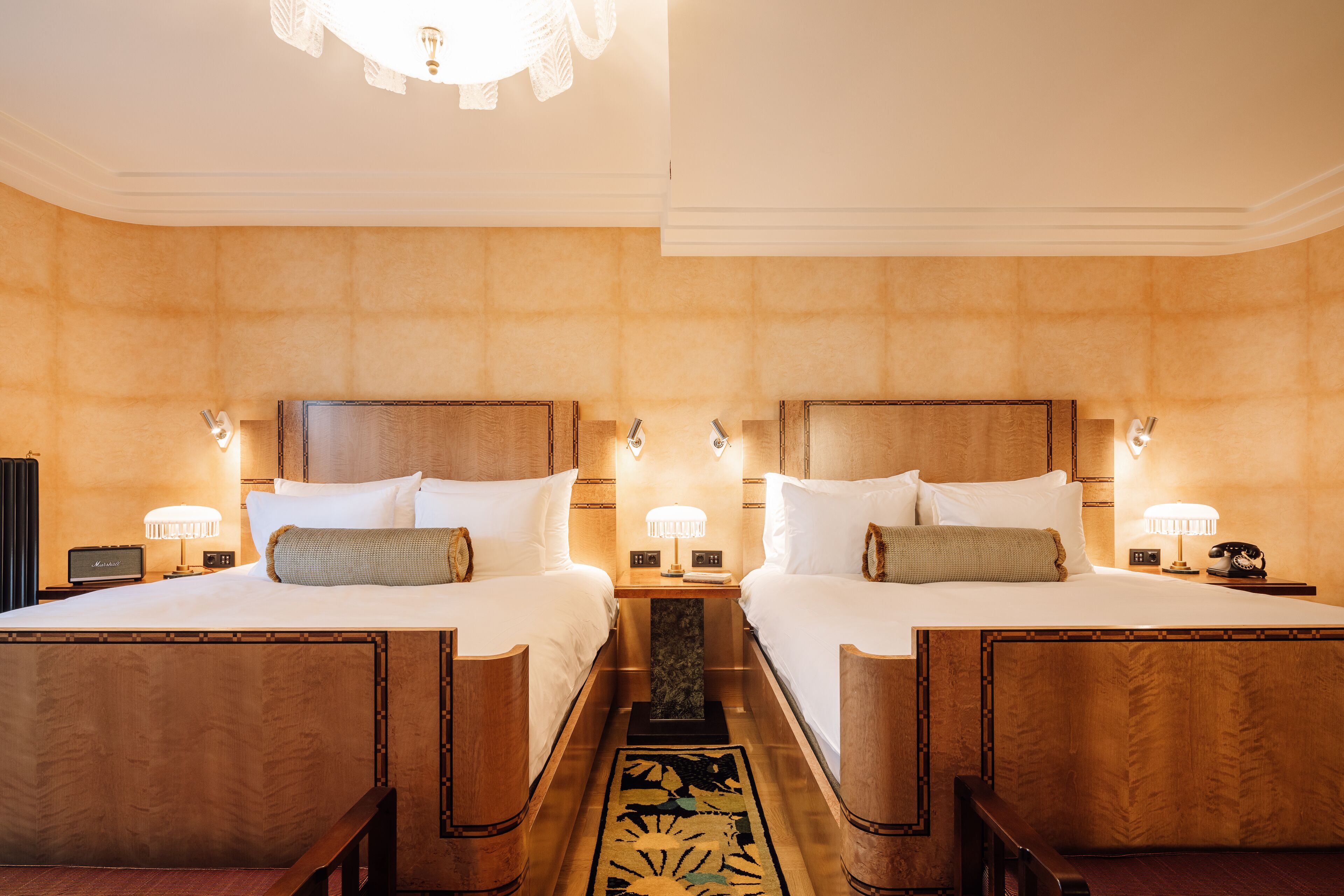 Ein Hotelzimmer mit zwei Betten, Holz-Kopfteilen, Nachttischen mit Lampen und einem dekorativen Teppich.