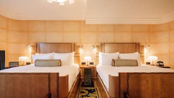 Ein Hotelzimmer mit zwei Betten, Holz-Kopfteilen, Nachttischen mit Lampen und einem dekorativen Teppich.