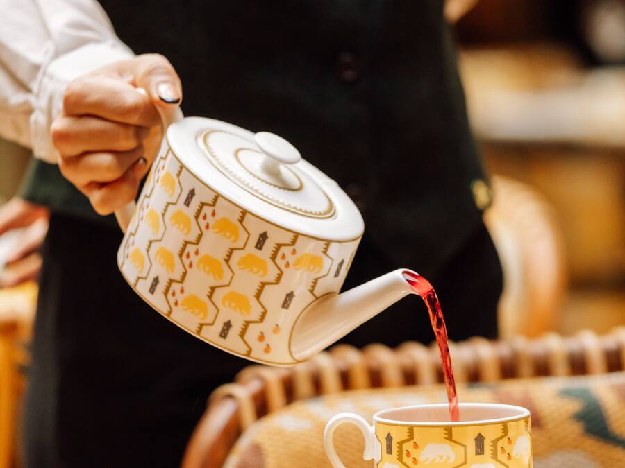 Una persona vertiendo té desde una tetera estampada en una taza a juego sobre un platito.