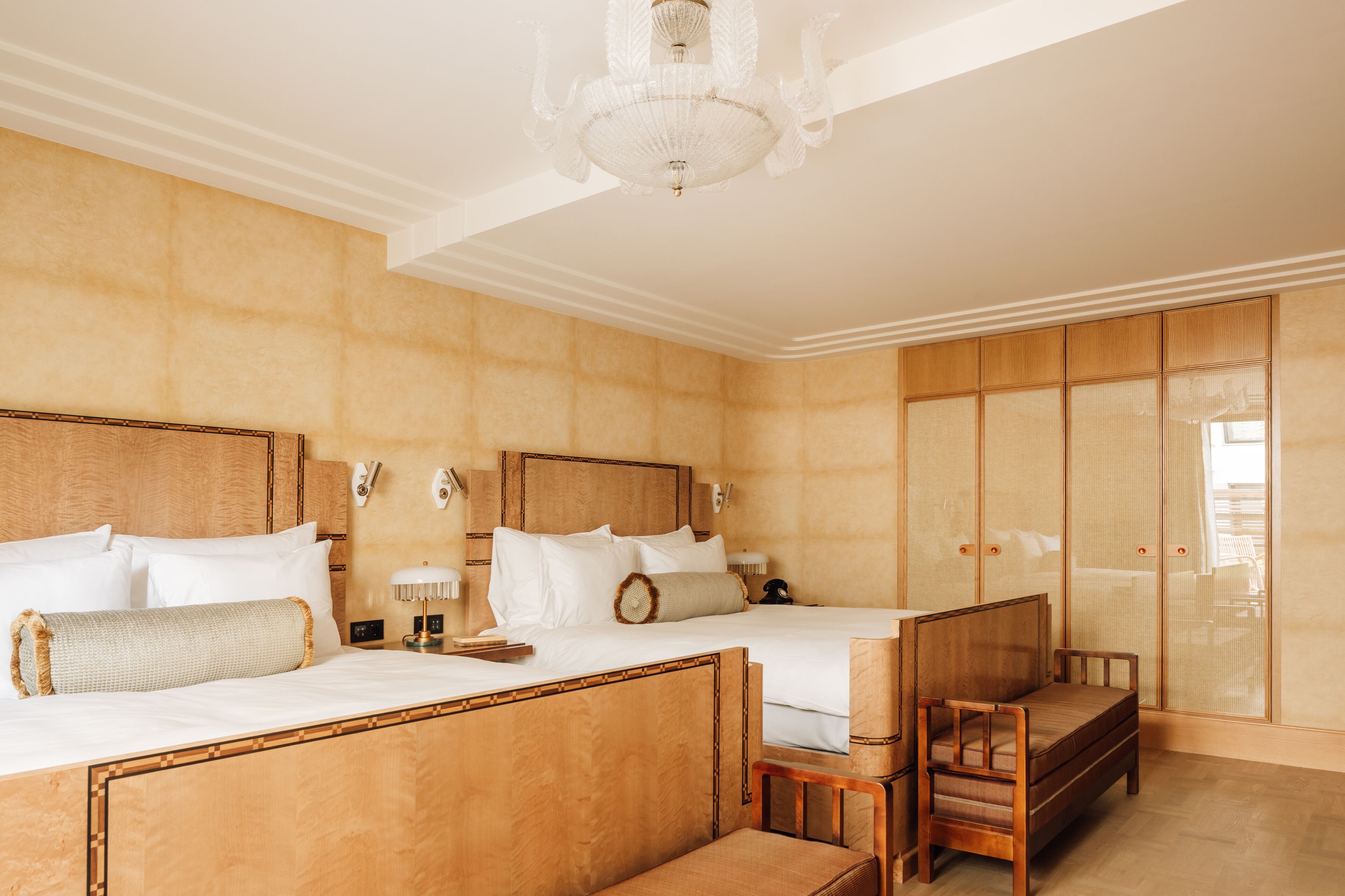 Habitación de hotel con dos camas, un armario de madera, un banco y una araña.