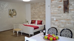 Un comedor con una mesa dispuesta para dos personas, un sofá blanco con cojines rojos, un taburete pequeño y una pared con diseño de piedra.