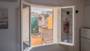 Quarto com uma janela ampla aberta, mostrando vista de edifícios próximos e uma varanda.